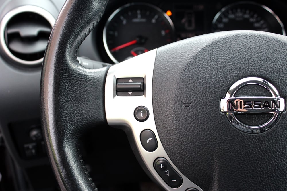 Closeup to a nissan steering wheel with a check engine light in the background