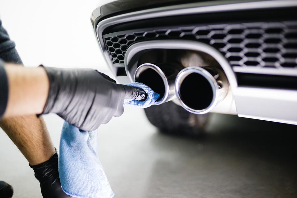An automotive technician cleaning a vehicle's exhaust with a rag