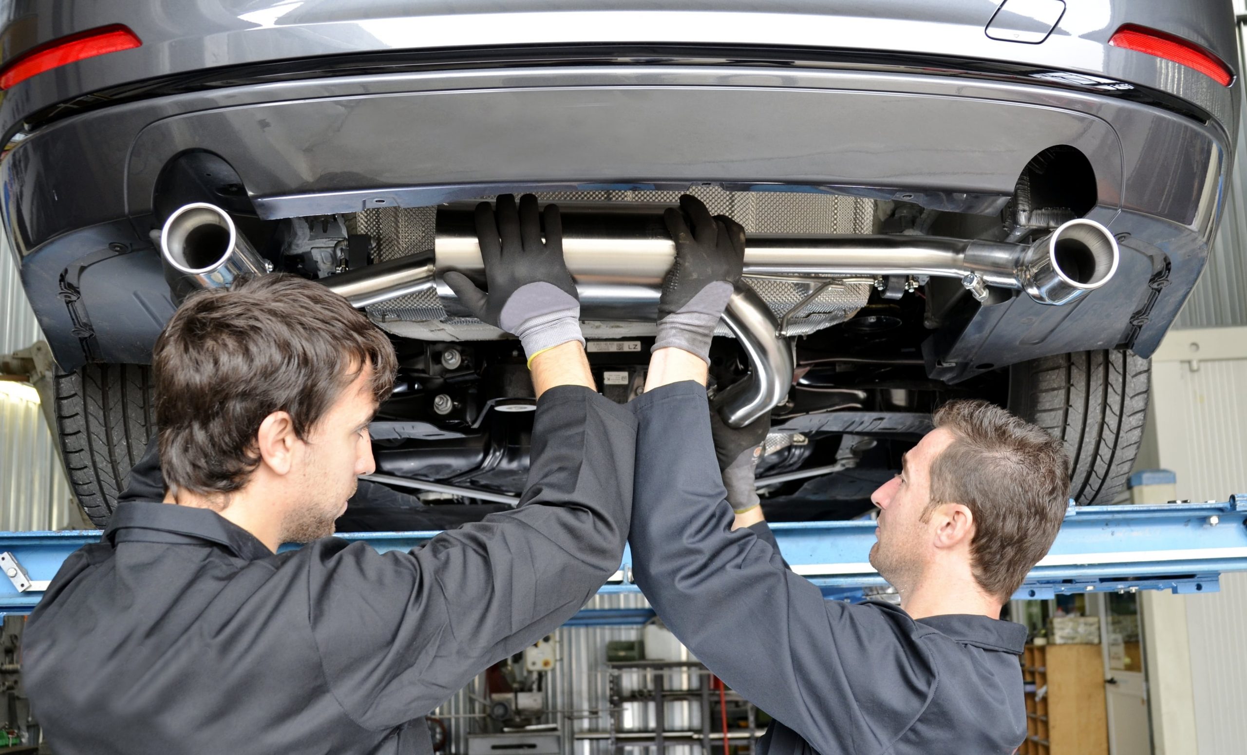 Two automotive technicians working together to install a new exhaust system