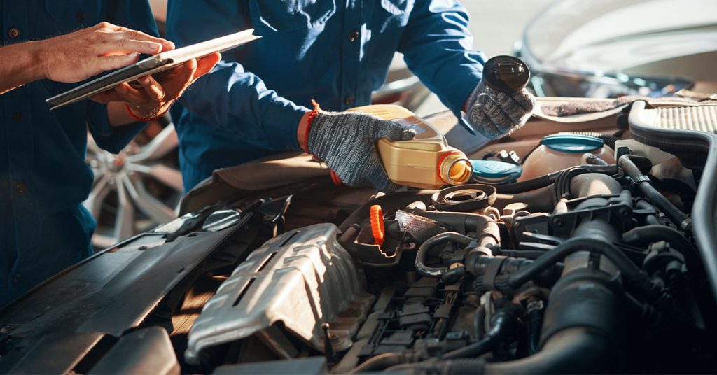 Two automotive technicians looking into the hood of a car, one with a tablet and the other inspecting the oil filter