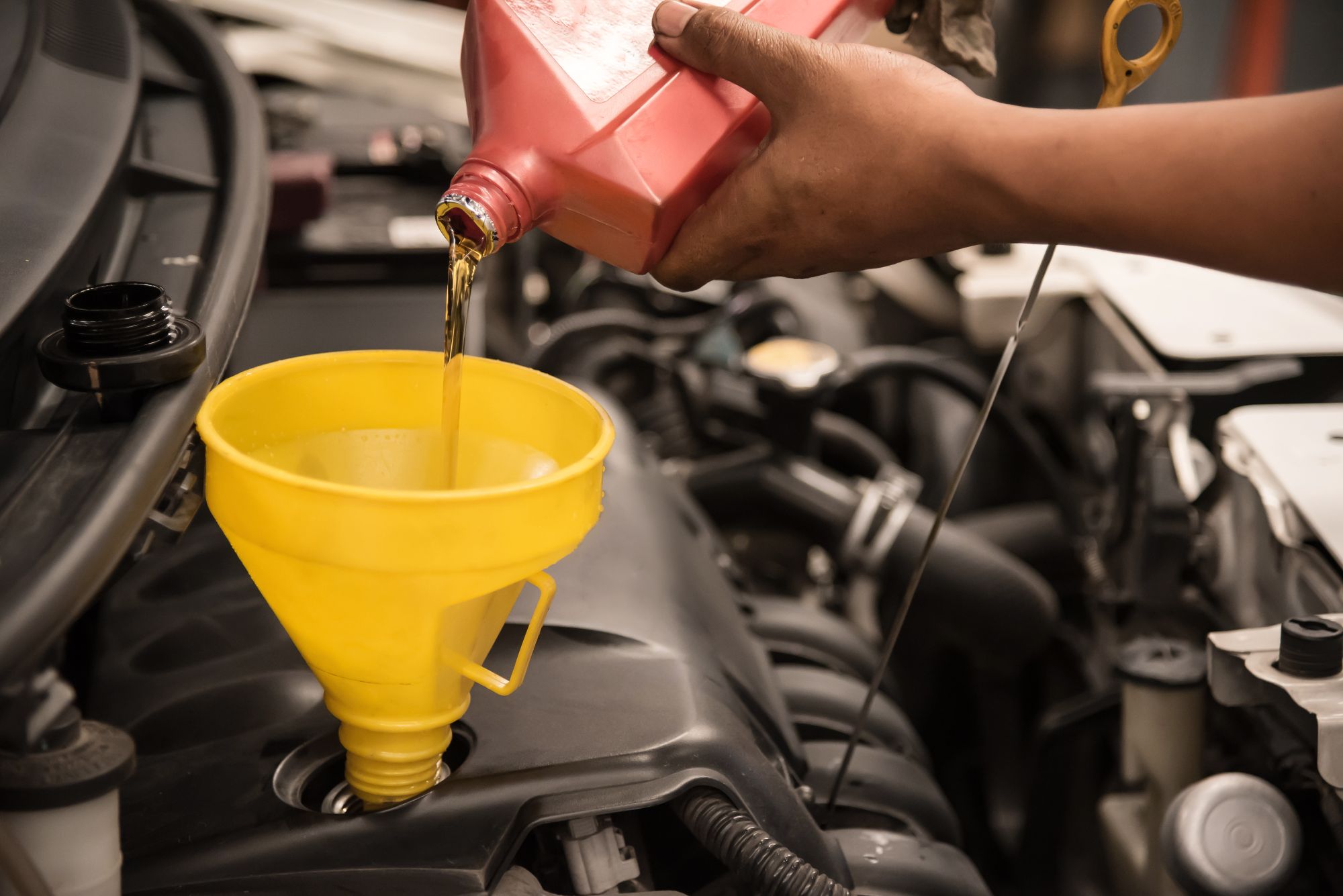 An automotive technician pouring oil into a vehicle with a funnel