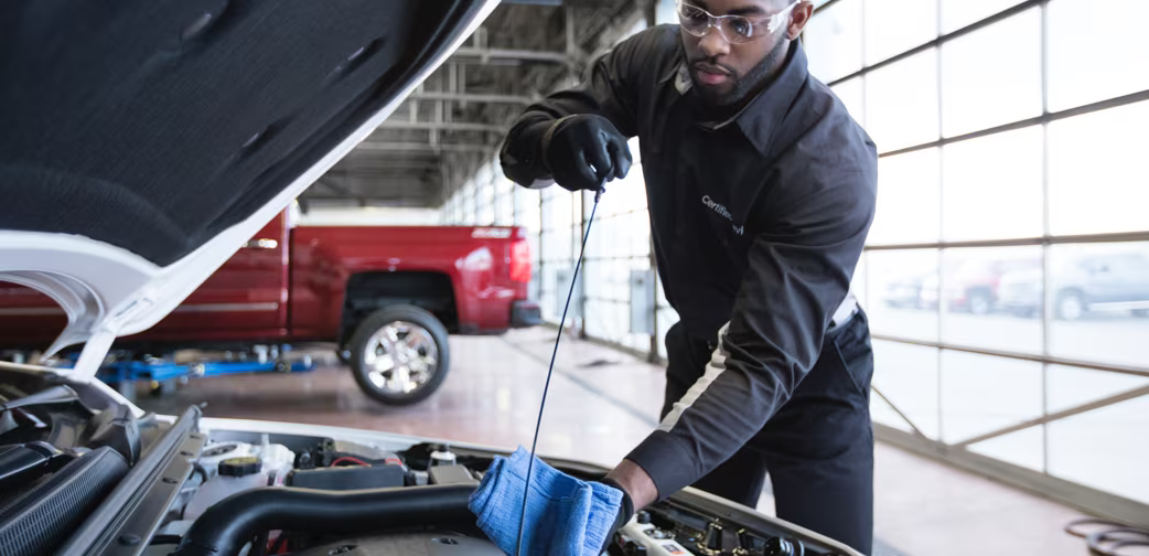 An automotive technician checking the oil level with a dipstick and a rag