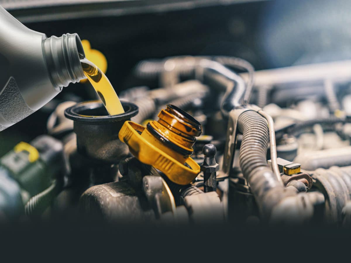 A closeup of an automotive technician pouring oil into a vehicle