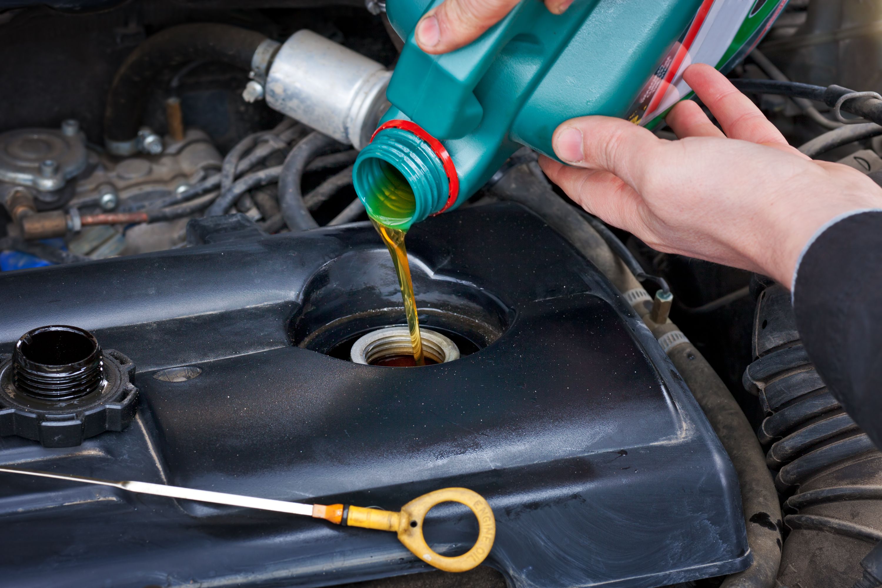 A closeup of an automotive technician refilling oil