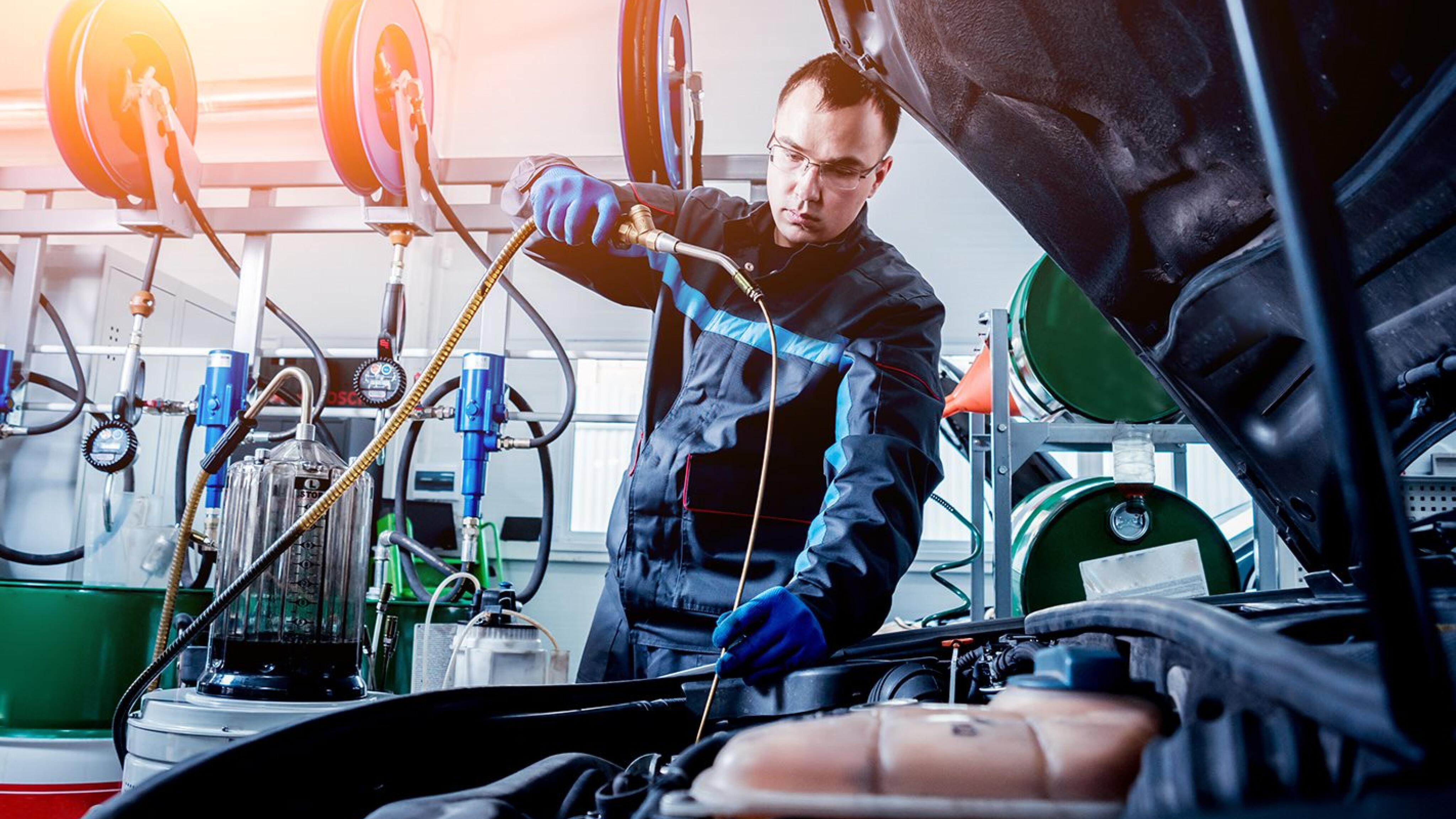 An automotive technician using a long tube to refill oil