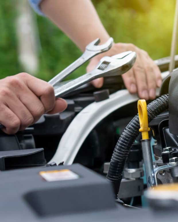 A closeup of an automotive technician holding two wrenches over the hood of a car