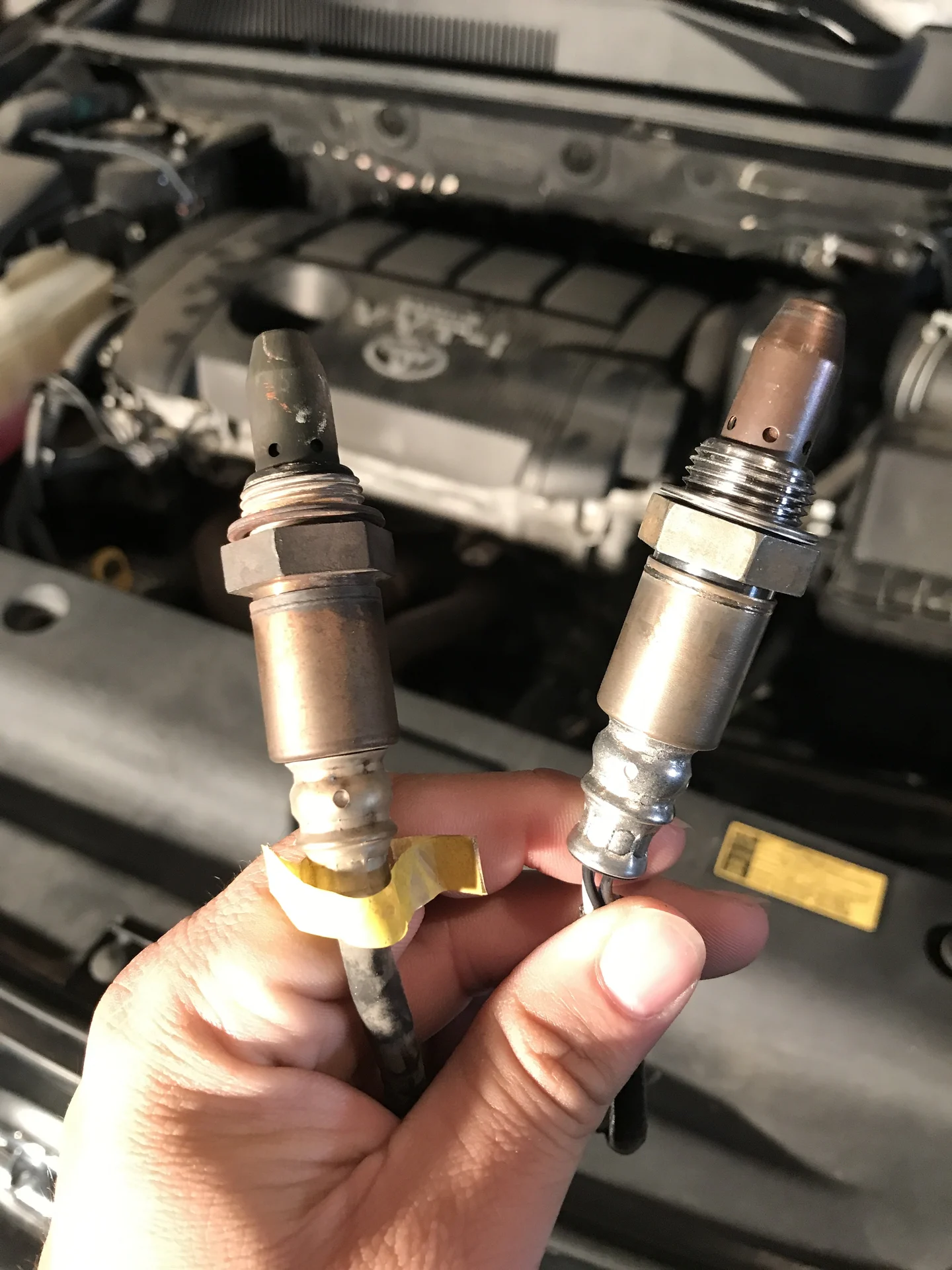 An automotive technician holding two oxygen sensors up to the camera