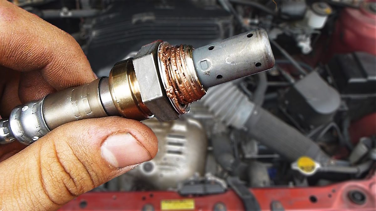 An automotive technician holding an oxygen sensor up to the camera