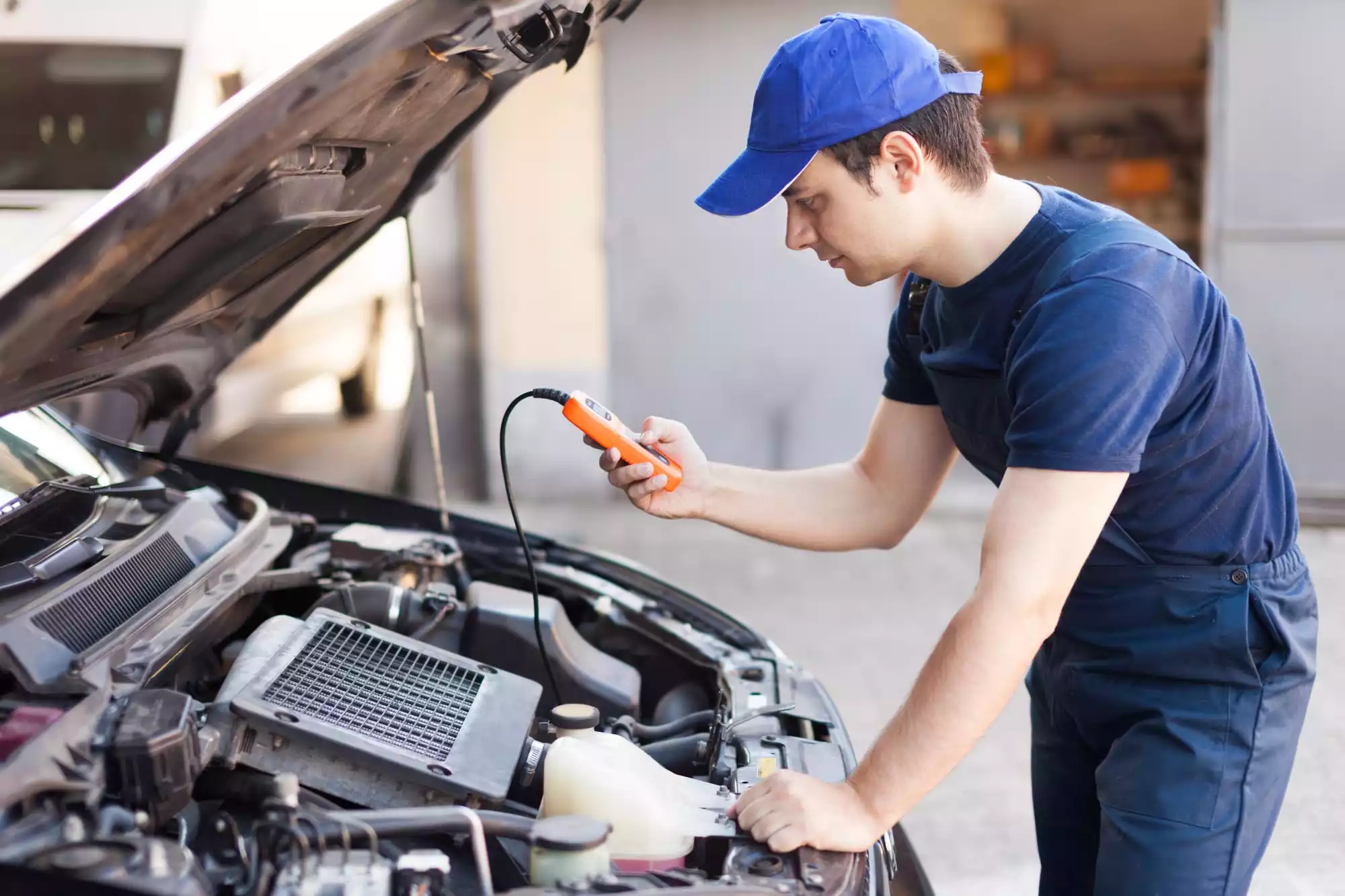 An automotive technician inspecting a vehicle with the hood open