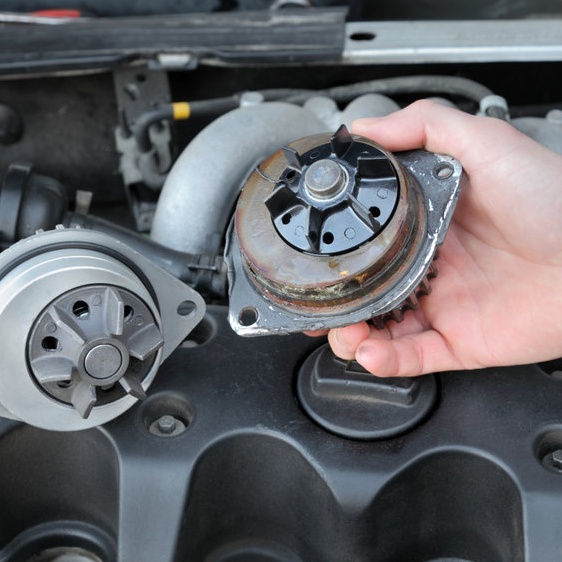 An automotive technician holding a water pump over a vehicle