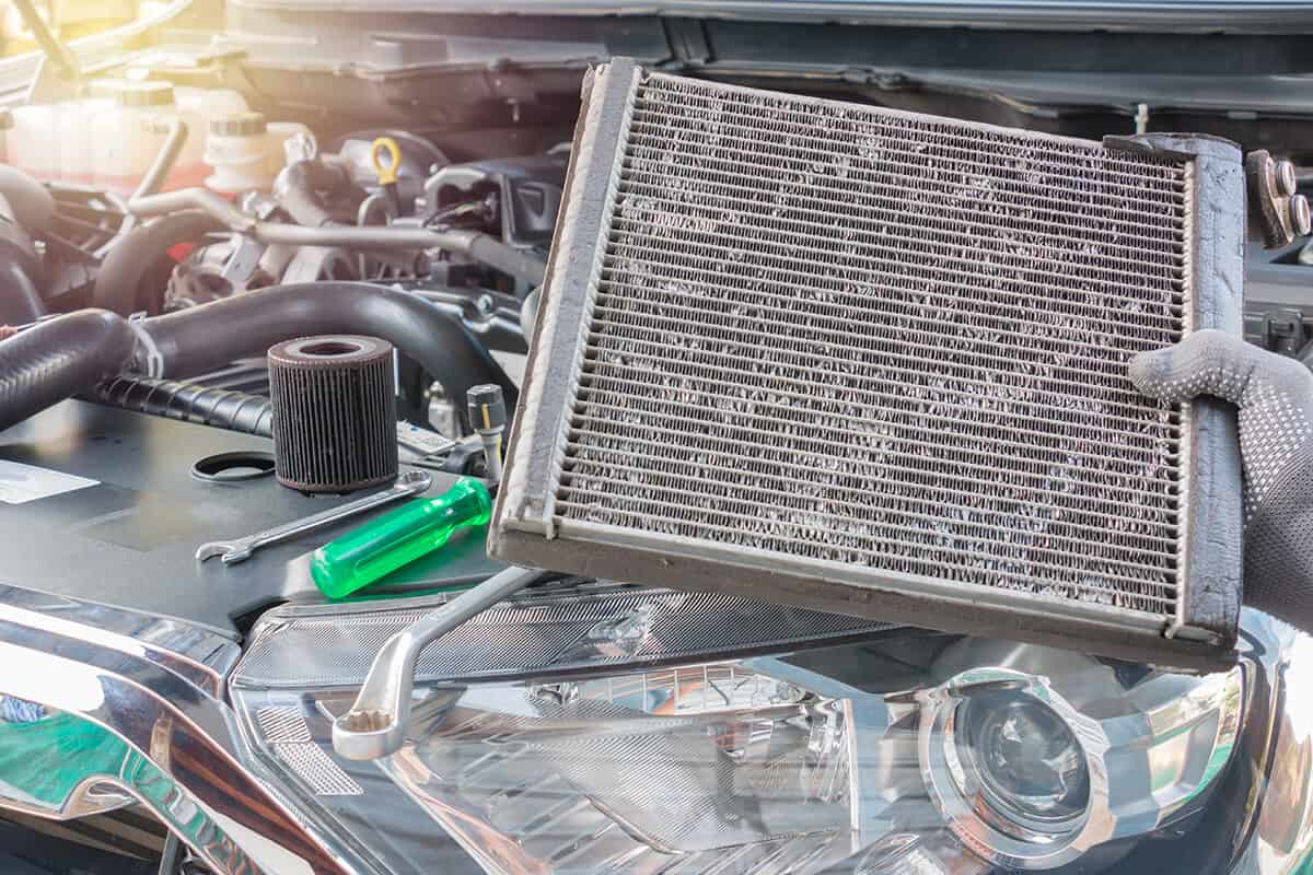 An automotive technician holding a radiator above a vehicle