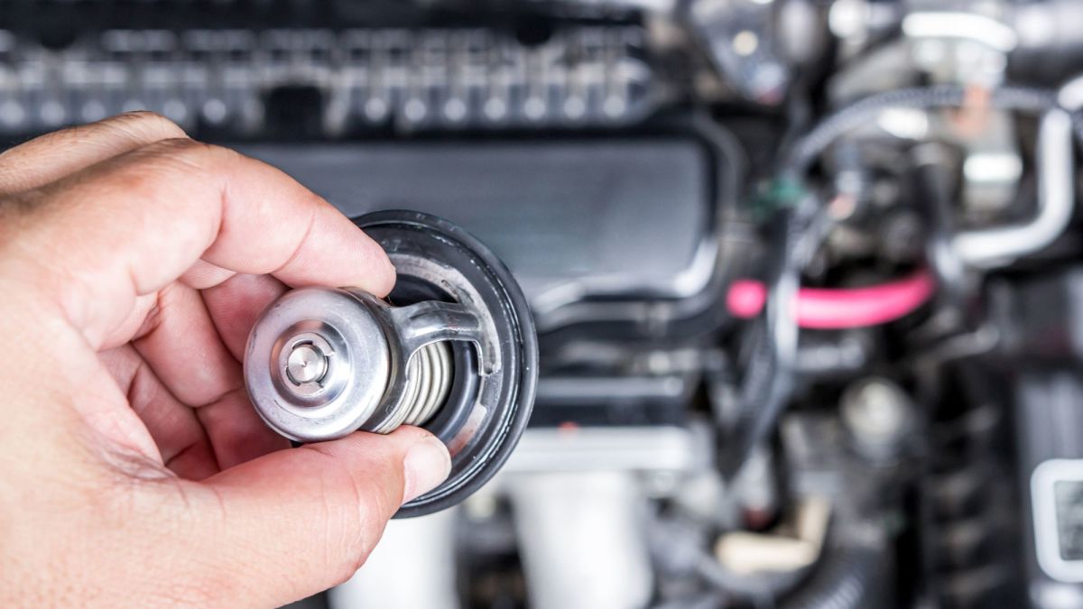 An automotive technician holding a thermostat