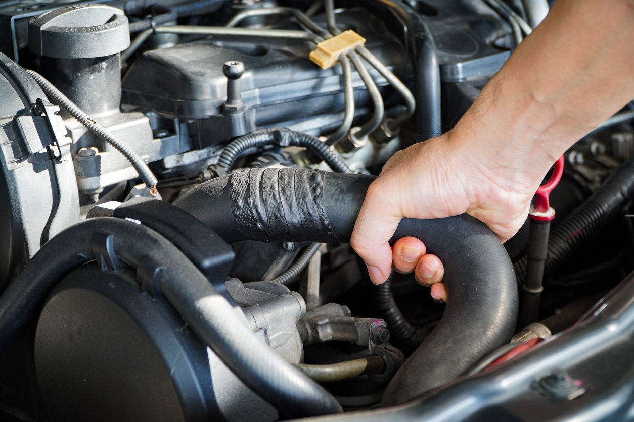 An automotive technician holding a hose with tape wrapped around to cover holes