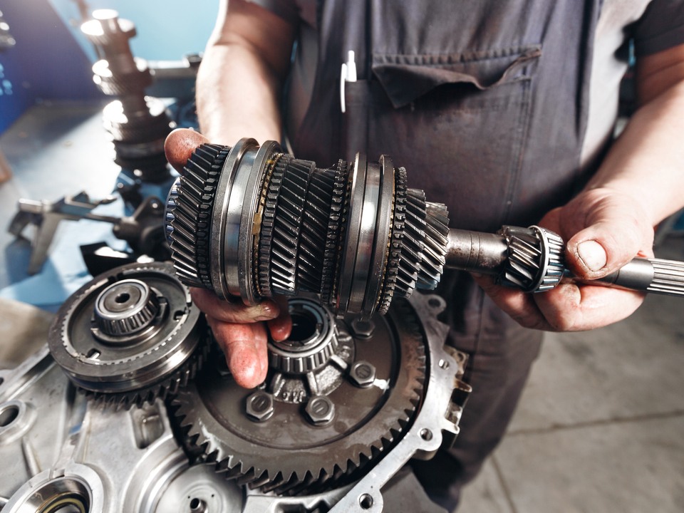 An automotive technician holding the internals of a transmission up to the camera