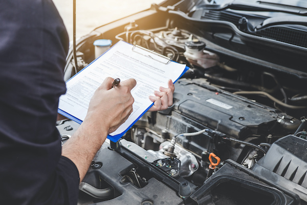 An automotive technician holding a clipboard while inspecting a vehicle's internals