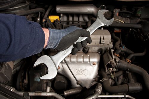 An automotive technician holding a wrench over a vehicle's internals