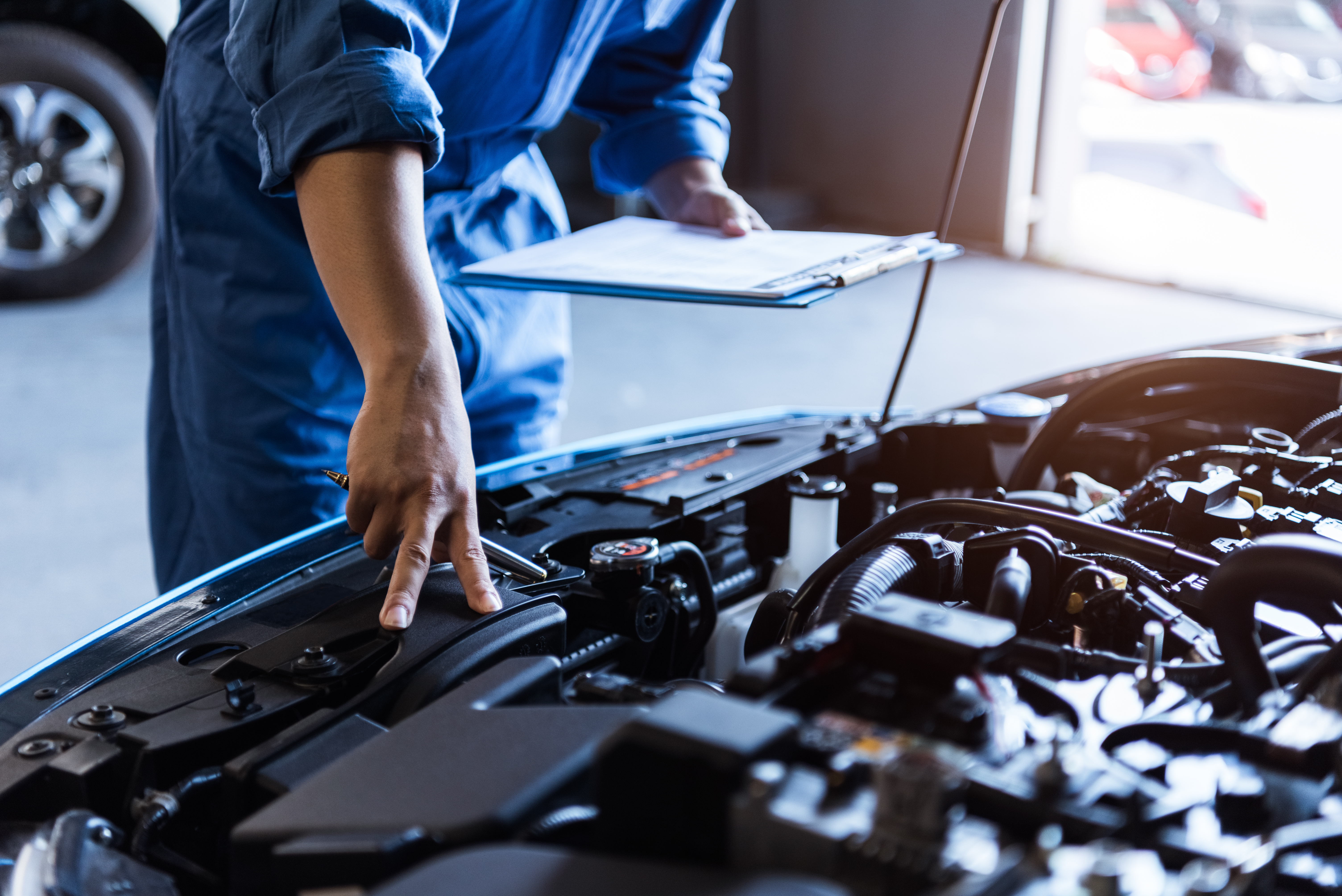 An automotive technician holding a clipboard while inspecting a vehicle's internals