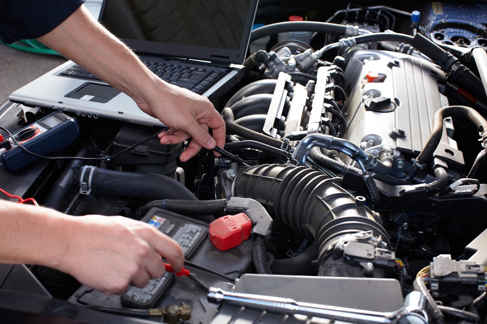 An automotive technician checking voltage with a multimeter and computer