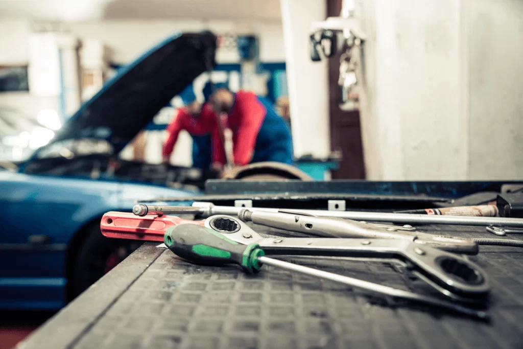 A closeup of some of the tools used to perform a tune up with automotive technicians in the background