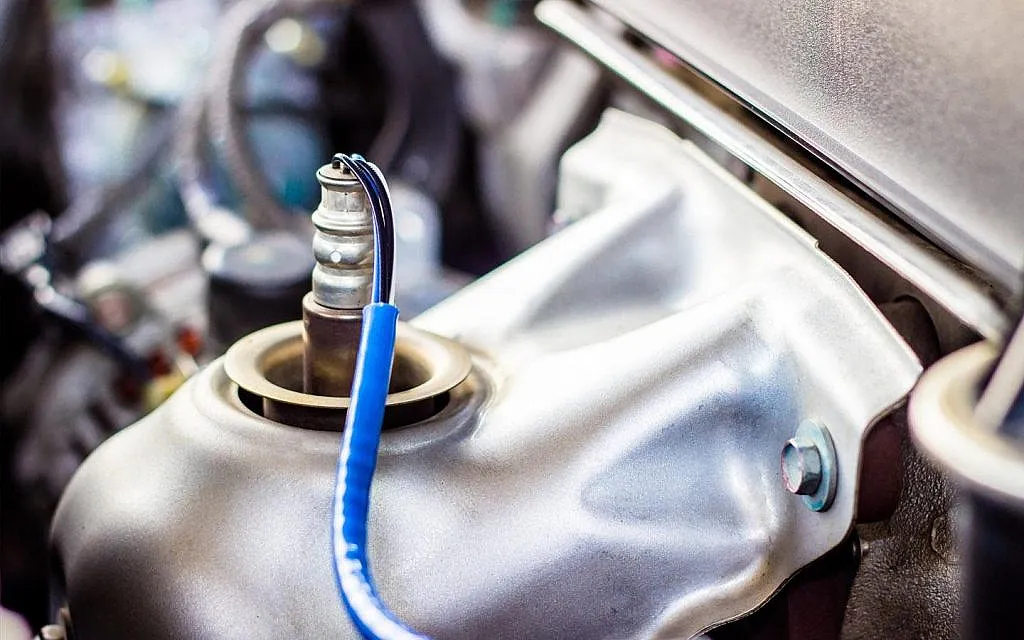 Oxygen sensor being replaced on a vehicle exhaust manifold during emissions service